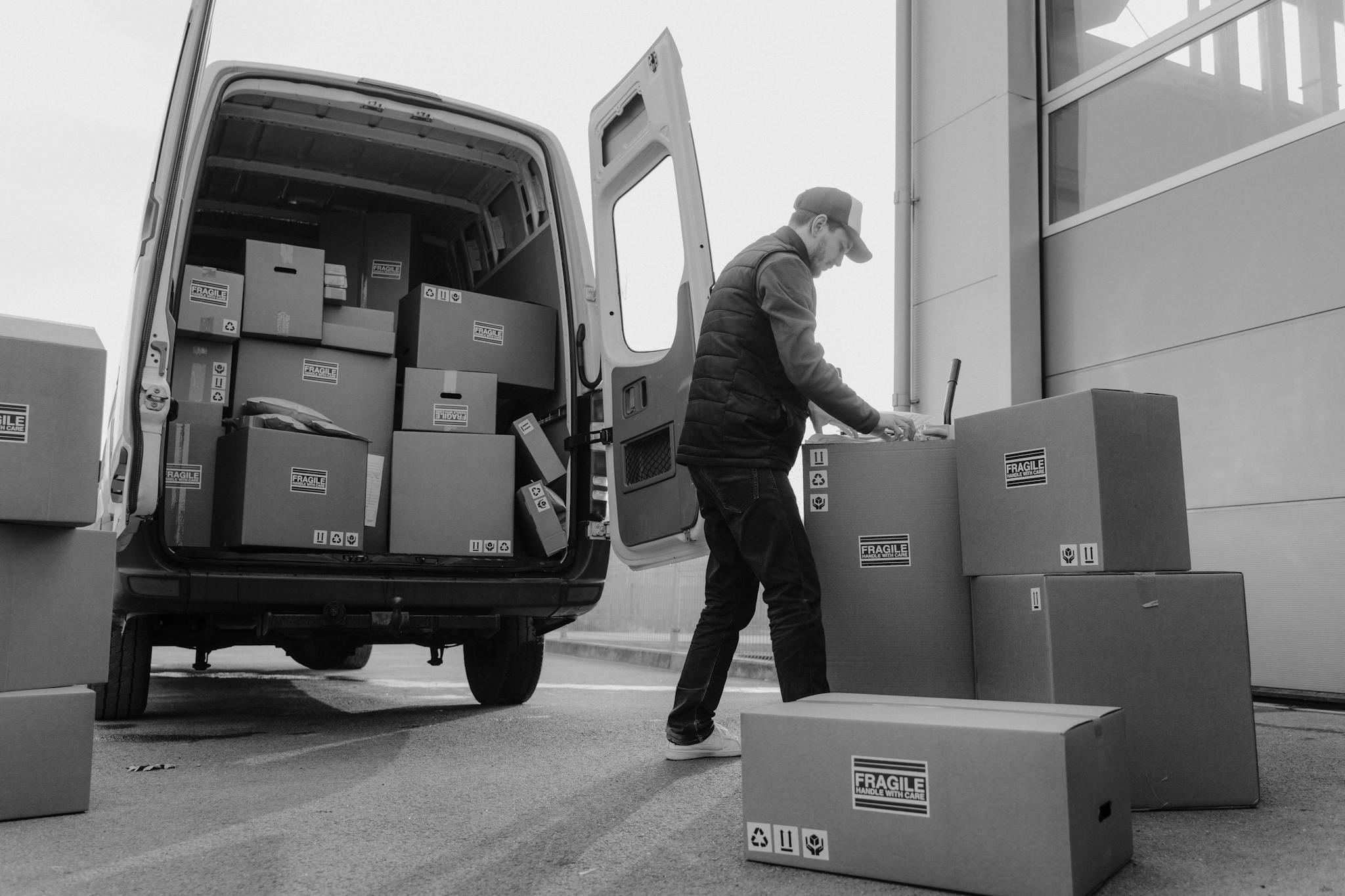 Grayscale Photo of Delivery Man Checking the Cardboard Boxes